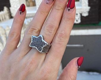 May include: A silver ring featuring a large, five-pointed star design. The star is set with small, black cubic zirconia stones.