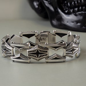 May include: A silver bracelet featuring a star-shaped design with intricate detailing. The bracelet is made of linked metal pieces and has a clasp closure. The back of the bracelet is engraved with the words "Bikers Yeti Jewelry".