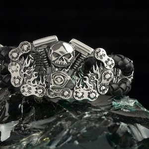 May include: A silver motorcycle engine bracelet with a skull and flames design. The bracelet is made of leather and metal and features a chain link detail.