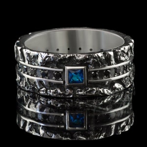 May include: A silver ring with a textured band and black diamonds. A blue gemstone is set in the center of the ring.