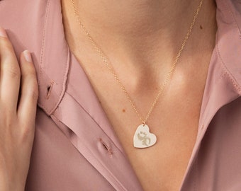 May include: A gold-colored necklace with a heart-shaped pendant. The pendant has a floral design and is suspended from a delicate chain. The chain length is 17 inches.