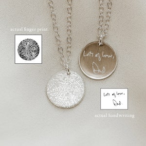 May include: Two silver necklaces with round pendants. One pendant has a fingerprint design and the other pendant has the words 'Lots of love, Dad' engraved on it. The pendant with the fingerprint design is shown next to a black and white image of a fingerprint. The pendant with the engraved message is shown next to a white piece of paper with the same message written in black ink.