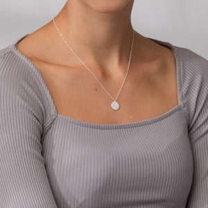 May include: A silver chain necklace with a small, round pendant. The chain is 18 inches long.