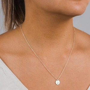 Woman wearing a personalized disc necklace engraved with a dog paw print. The gold filled pendant hangs on a dainty chain, sitting just below the collarbone. Showcases how the custom pet print necklace looks when worn—simple, elegant, and meaningful for pet lovers.
