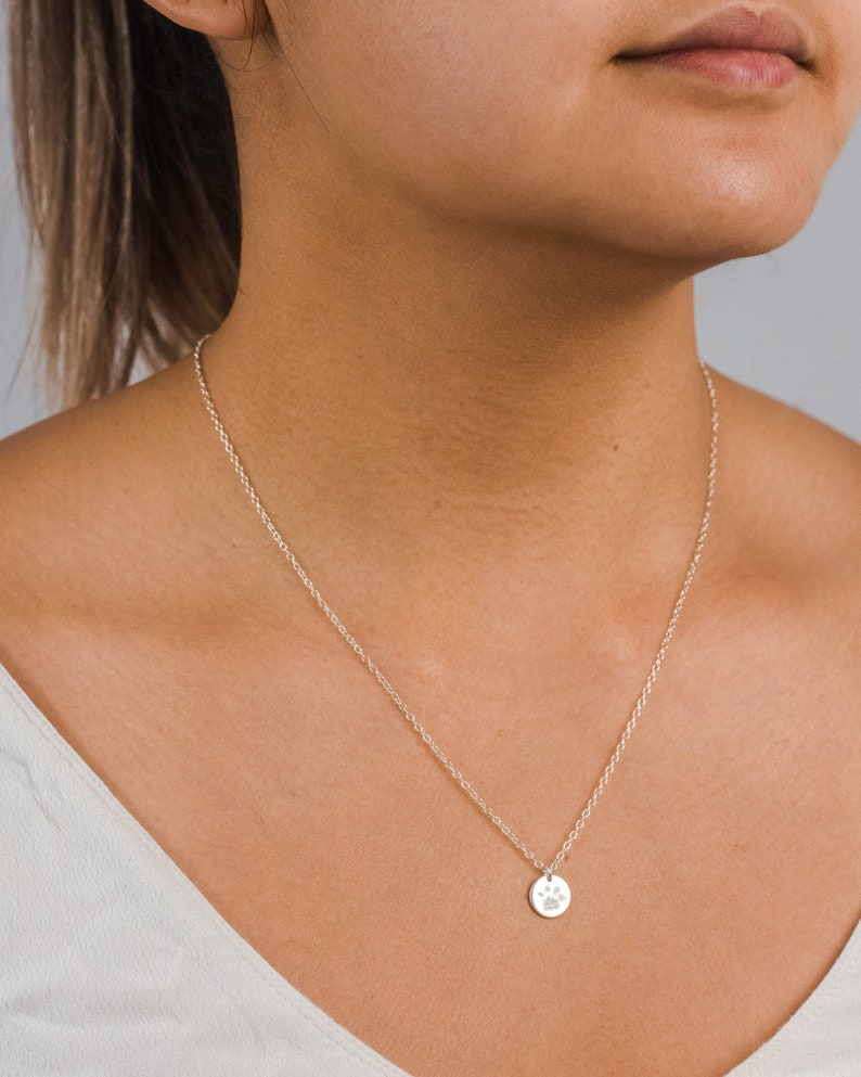 Woman wearing a personalized disc necklace engraved with a dog paw print. The gold filled pendant hangs on a dainty chain, sitting just below the collarbone. Showcases how the custom pet print necklace looks when worn—simple, elegant, and meaningful for pet lovers.