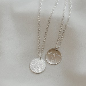 May include: Two silver necklaces with circular pendants. One pendant features a fingerprint design, the other has the handwritten message "Lots of love, Dad".