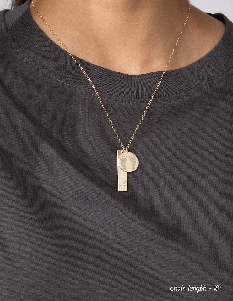 May include: Gold necklace with a small round pendant featuring a footprint design and a bar pendant with the text "the world is yours to explore". The chain is 18 inches long.