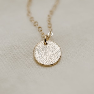 Peut inclure: Un collier en or avec un pendentif rond orné d'une empreinte digitale détaillée.