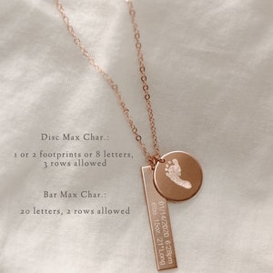 May include: A rose gold necklace with a small round disc charm and a rectangular bar charm. The disc charm has a footprint engraved on it. The bar charm has the text "01/14/2020 6:28pm 6lbs. 15oz. 21" Long" engraved on it. The necklace is on a white fabric background.