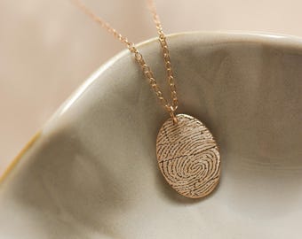 Peut inclure: Un collier en chaîne dorée avec un pendentif en forme d'empreinte digitale. Le pendentif est ovale et présente un design détaillé.