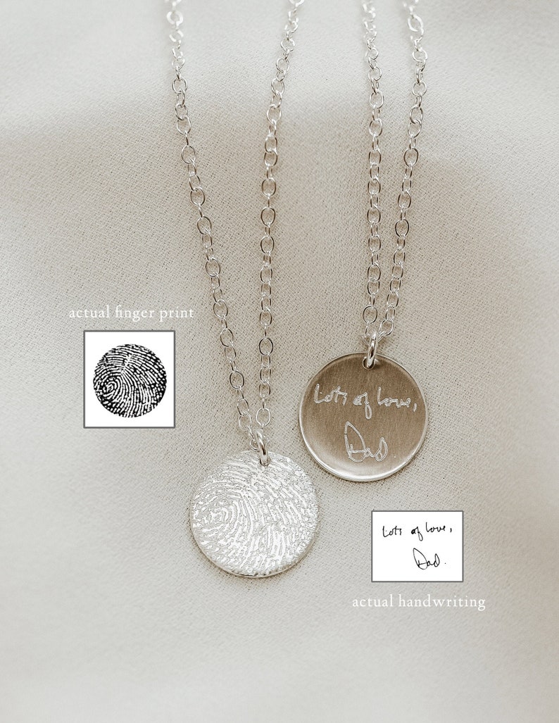 May include: Two silver necklaces with round pendants. One pendant has a fingerprint design and the other pendant has the words 'Lots of love, Dad' engraved on it. The pendant with the fingerprint design is shown next to a black and white image of a fingerprint. The pendant with the engraved message is shown next to a white piece of paper with the same message written in black ink.