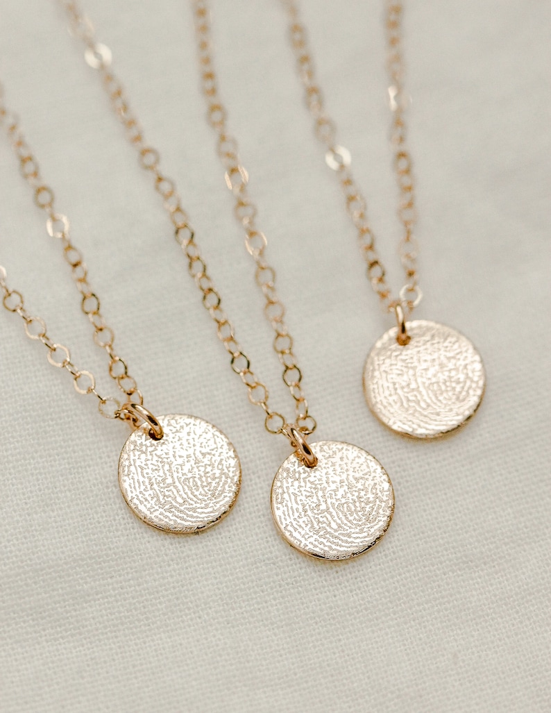 Puede incluir: Tres collares de oro con colgantes redondos que presentan un dise&ntilde;o de huella digital texturizado.