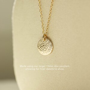 Pode incluir: Colar dourado com um pendente de disco texturizado de 13 mm. O pendente pende de uma corrente delicada. O texto na imagem diz: "Made using our larger 13mm disc pendant, allowing for finer details to show."
