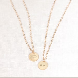 May include: Two gold necklaces with round pendants. The pendant on the left says "Molly 06/23/20". The pendant on the right says "Luna".