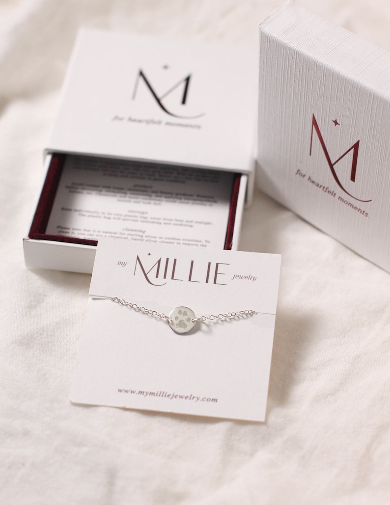 Gift-ready paw print bracelet packaged in a jewelry box. The delicate bracelet features a custom engraved pet paw print charm, displayed neatly on a soft insert with tissue or ribbon. Perfect for gifting as a personalized keepsake or memorial jewelry piece for pet lovers.