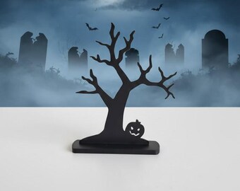 Può includere: Silhouette nera di un albero a tema Halloween con una zucca intagliata alla base. Lo sfondo presenta una scena spettrale di cimitero con luna piena, pipistrelli e nebbia. Decorazione perfetta per Halloween.