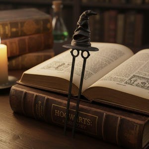 May include: A black metal bookmark shaped like the Sorting Hat from the Harry Potter series, resting on an open book. The book is titled "Hogwarts: A History". The background includes other books and a candle.