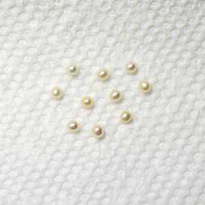 May include: A collection of ten white pearls of various sizes, arranged in a heart shape on a white textured surface.