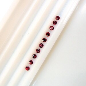 Peut inclure: Une rangée de 12 petites pierres précieuses rondes rouges sur une surface blanche.