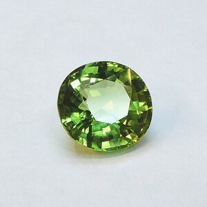 May include: A round, green peridot gemstone with a faceted cut. The stone is set against a white background.