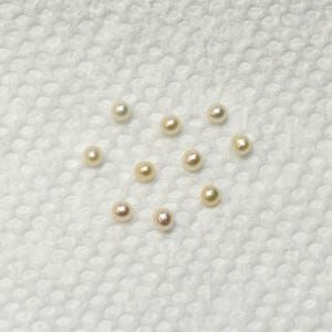 May include: A collection of 10 white and cream colored pearls on a white surface.