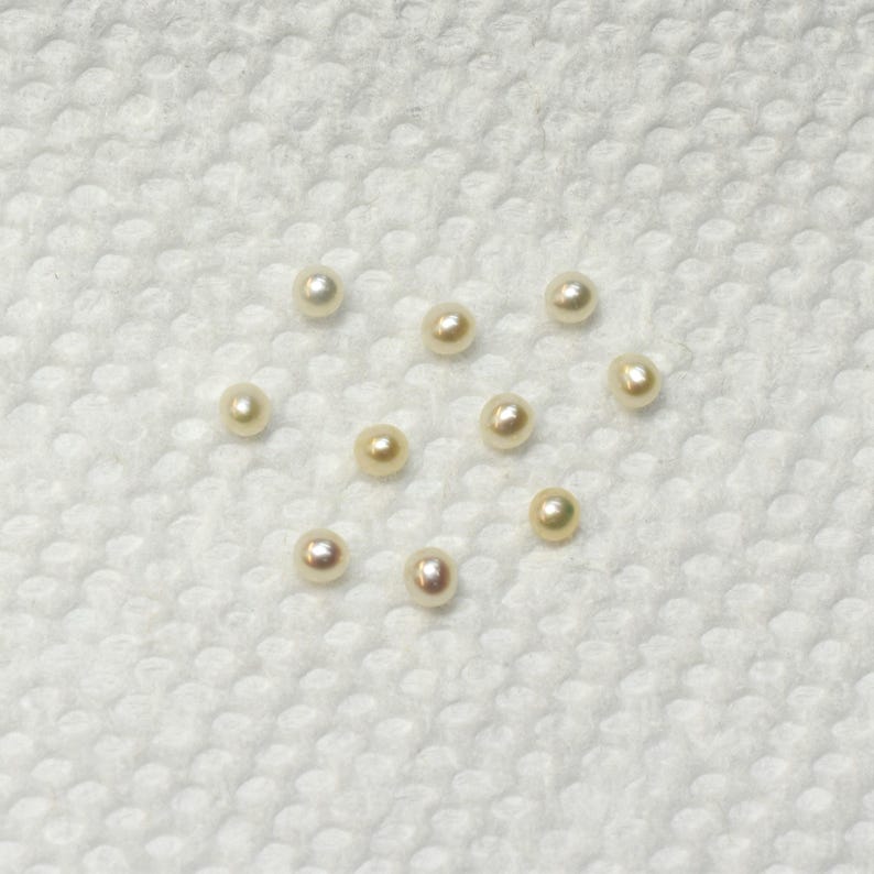 May include: A collection of 10 white and cream colored pearls on a white surface.