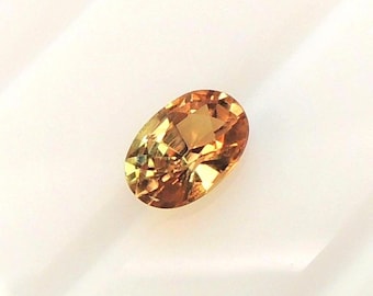 Oval golden yellow sapphire measuring 4.5 x 6.6 mm, this corundum weighs 0.82 carats; this orange-yellow stone has a metallic appearance.