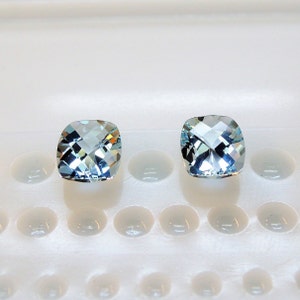 Puede incluir: Dos piedras preciosas de talla coj&iacute;n de color azul claro sobre un fondo blanco.
