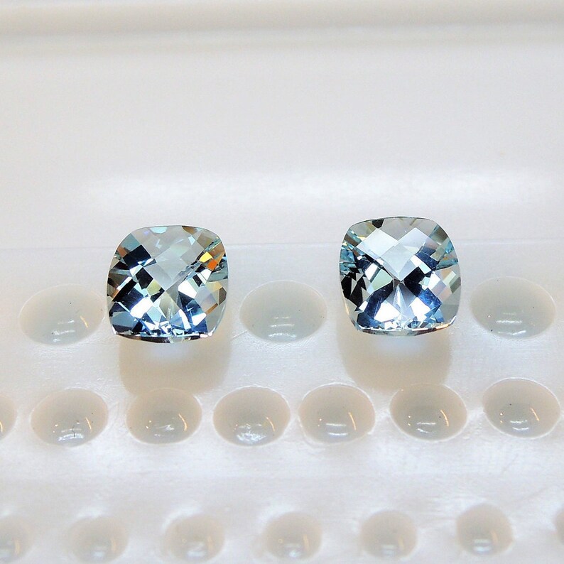 Puede incluir: Dos piedras preciosas de talla coj&iacute;n de color azul claro sobre un fondo blanco.