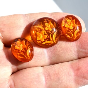 May include: Three amber-colored glass buttons with floral designs. The buttons feature a raised design of flowers and leaves.