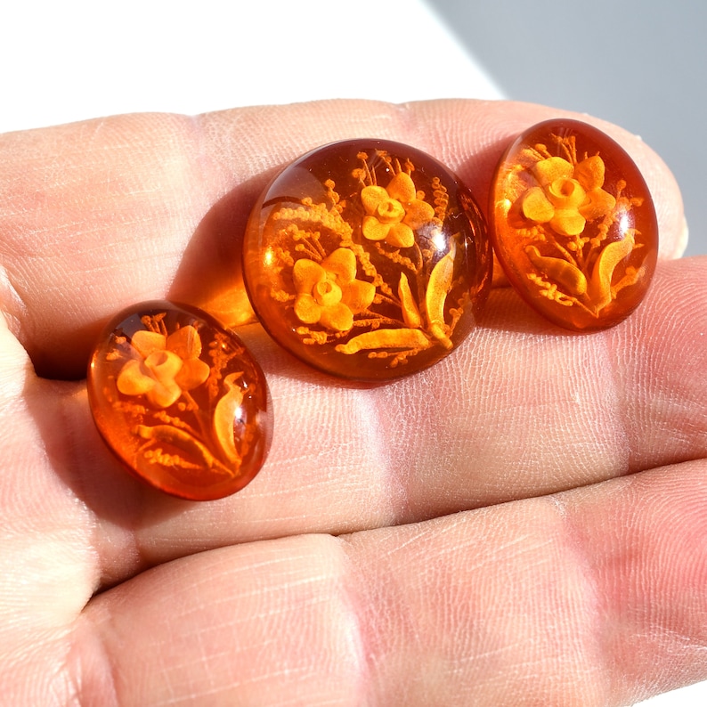 May include: Three amber-colored glass buttons with floral designs. The buttons feature a raised design of flowers and leaves.