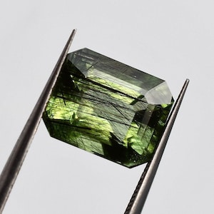 Gray green peridot with black tourmaline needles, this large olivine from Pakistan with emerald cut measures 11x9 mm and weighs 5.90 carat