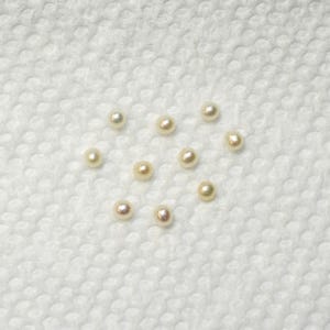 May include: A collection of 10 white pearls on a white textured surface.