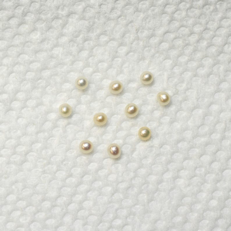 May include: A collection of 10 white pearls on a white textured surface.