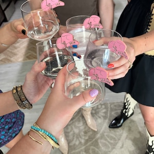 May include: Five clear glass cups with pink cowboy hat shaped drink markers. The markers have the names "LEA", "JENNY", "ERIN", "MADDOX", and "TAYLOR" written on them.