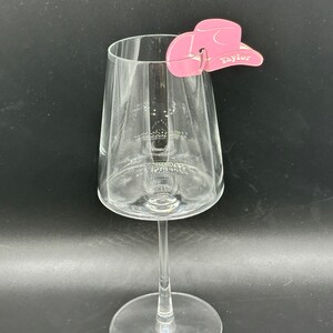 May include: Pink cowboy hat shaped wine glass charm with the name "Taylor" written on it.