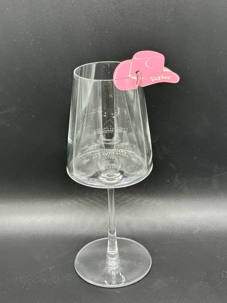 May include: Pink cowboy hat shaped wine glass charm with the name "Taylor" written on it.