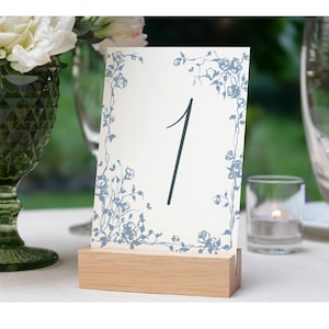 May include: A white table number card with a blue floral design and the number "1" printed in black. The card is on a wooden stand.