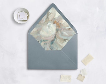 May include: A gray envelope with a floral patterned interior, surrounded by small white stamps and a small bowl of stamps. The envelope's interior features a soft, abstract design in shades of white, pink, and blue.