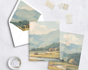 May include: Stationery set featuring a watercolor landscape design. The set includes an envelope, notecards, and stamps. The artwork depicts a serene valley with mountains, trees, and a river, rendered in soft blues, greens, and yellows.
