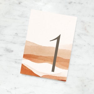 May include: A rectangular table number card featuring a watercolor design in shades of orange and brown, resembling a landscape. A large, dark gray number 1 is centered on the card. The card has a clean, minimalist aesthetic.