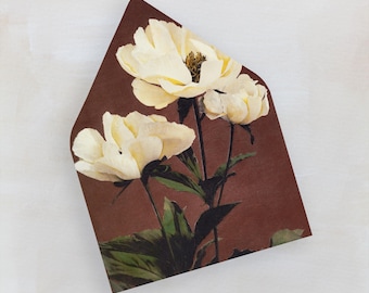 May include: An envelope with a brown background featuring a floral design of three white peony flowers with green leaves and stems. The envelope is a unique shape, with a pointed top.