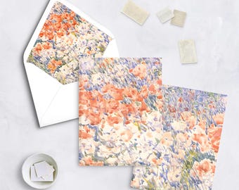 May include: Stationery set featuring floral watercolor designs. Includes two cards, an envelope with a floral interior, and stamps. The cards and envelope showcase a pattern of peach, white, and blue flowers, evoking a field of blooms.