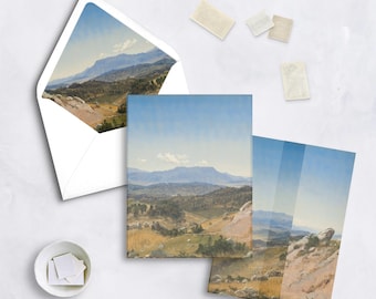 May include: Greeting cards featuring a landscape painting of a mountain range under a blue sky. The image includes an envelope with the same artwork, along with several stamps and a small dish of stamps.