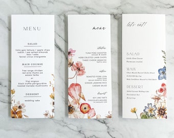 May include: A wedding menu with floral illustrations. The menu includes a salad, main course, and dessert. The salad includes little gem lettuce, apple chips, radish, sea salted almonds, feta, saba, and fennel citrus vinaigrette. The main course includes free range chicken with red wine thyme jus and estate herbs, or filet mignon with black truffle perigourdine and roasted maitake mushrooms. The dessert is wedding cake.