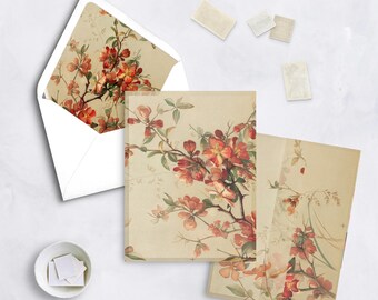 May include: Stationery set featuring floral illustrations. The set includes a white envelope, notecards, and stamps. The cards and envelope are adorned with a vintage-style design of red and orange blossoms on branches, set against a cream background.