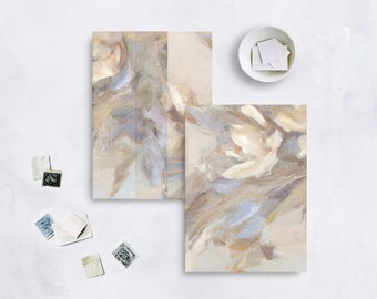 May include: Two abstract art prints with floral designs in neutral tones of beige, brown, and blue. A small white bowl holds several white squares, and several vintage stamps are scattered nearby.