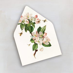 May include: White envelope featuring a botanical illustration of apple blossoms and green leaves. The design includes several bees in flight, with pink and white flowers on a brown branch. The envelope has a pointed flap.