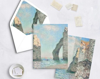 May include: Stationery set featuring a reproduction of a seascape painting. The set includes a white envelope, notecards, and stamps. The artwork depicts a coastal scene with a rock arch, blue water, and a light blue sky.