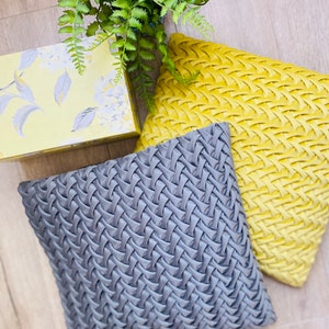 May include: Two decorative throw pillows, one gray and one yellow, with a woven pattern. The pillows are on a wooden floor.